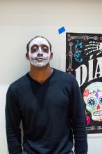 A student with his face painted poses with the Dia de los muertos sign