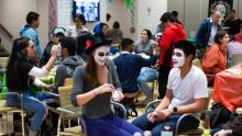 Smiling participants paint one another's faces in Day of the Dead style